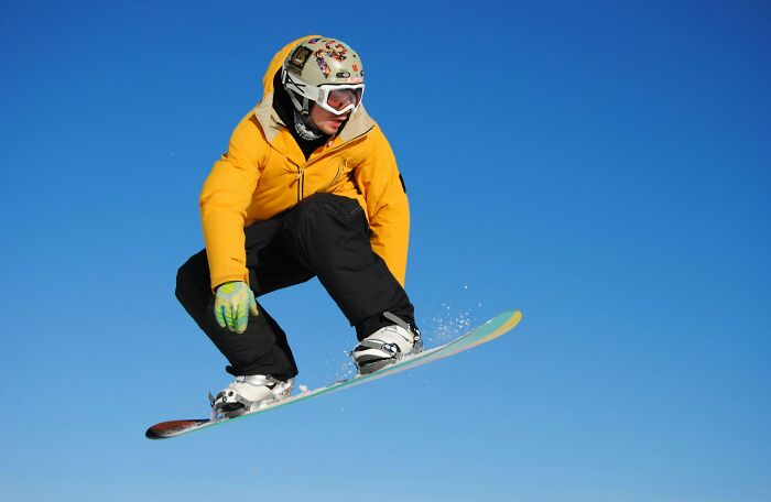Snowboarder in a yellow jacket catching air against clear sky, illustrating random life decisions leading to the right place.