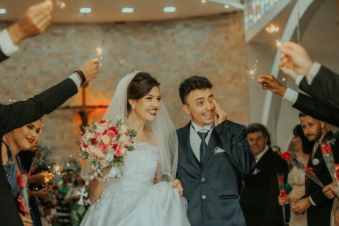 A smiling bride and emotional groom walk through a church aisle, surrounded by guests holding sparklers, illustrating breaking points.