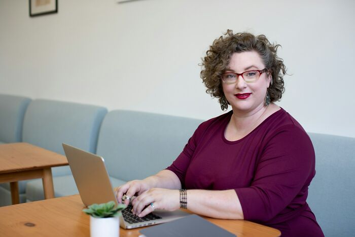 Woman with curly hair and glasses typing on a laptop, illustrating stories about former bullies from childhood.