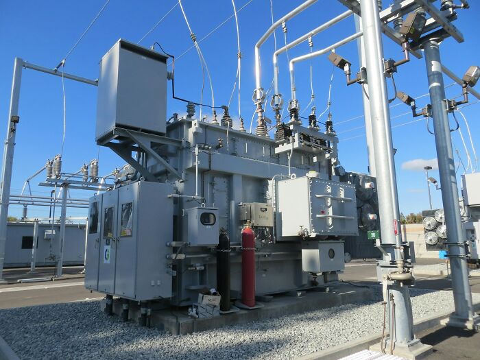 Outdoor electrical transformer station with power lines and industrial equipment under a clear blue sky.