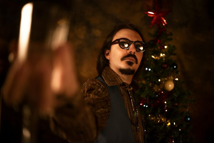 Man with glasses and goatee in front of a Christmas tree. He's sharing brutally honest stories about celebrity relatives.