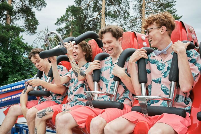 Four young men wearing matching outfits laughing on an amusement ride, capturing wild bachelor party moments outdoors.