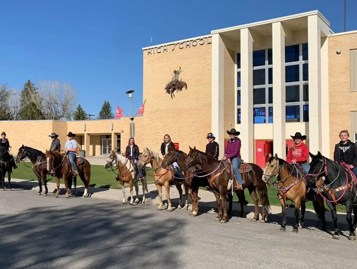 Students on horseback, dressed in cowboy hats, posing in front of their high school. An animal photo with good vibes.