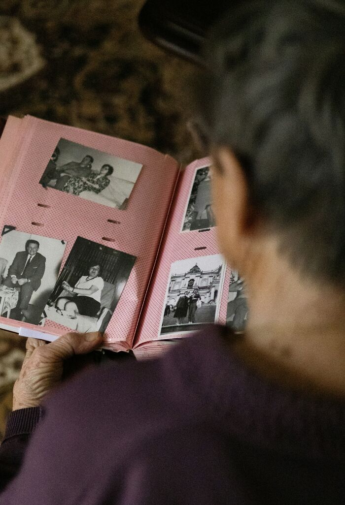A person's head from behind, looking at an open photo album. Old black and white family photos reveal family secrets and memories.
