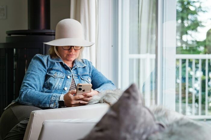 Woman in a wide-brimmed hat and denim jacket, intently looking at her phone. Reading stories about who had the worst MIL.