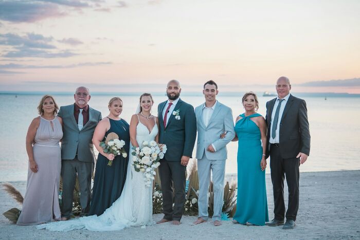 Group of wedding guests and couple posing on the beach, capturing moments of a wedding and future breakup insight.