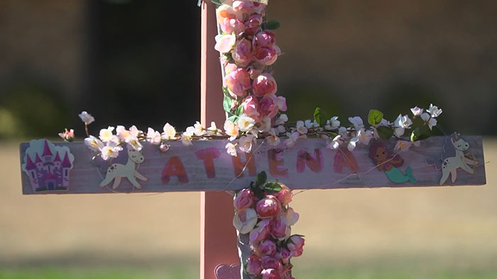 Memorial cross decorated with flowers and unicorns honoring Athena Strand, symbolizing a heartfelt court-related story.