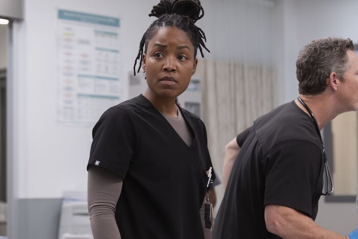 Female medical professional in black scrubs looks concerned in hospital setting, highlighting The Pitt major cast shake up before finale.