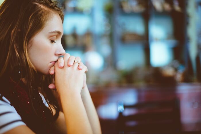 A pensive woman with closed eyes, hands clasped, perhaps reflecting on Worst MIL stories.