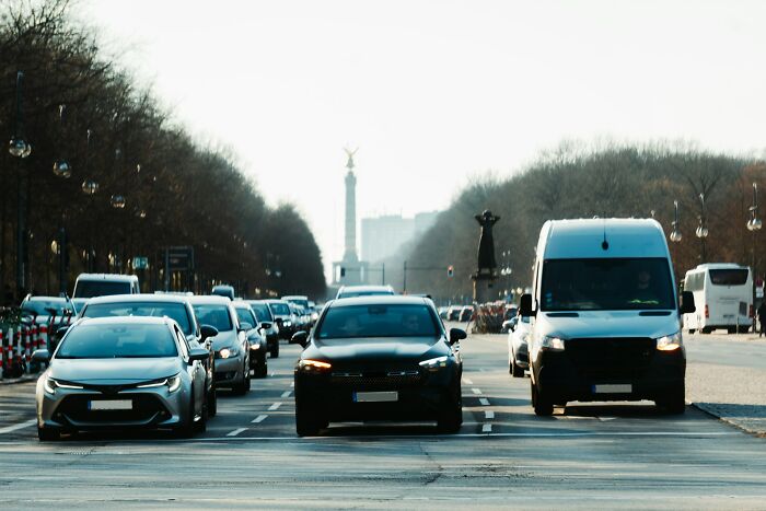 Several cars stopped on a busy city street with trees and a monument visible, illustrating karma in traffic situations.