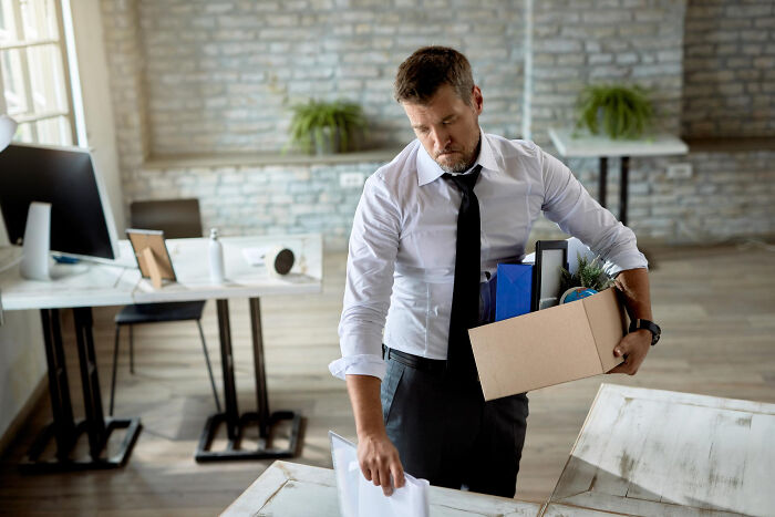 Man in office holding box of personal items, experiencing a real life plot twist at work during moving day.