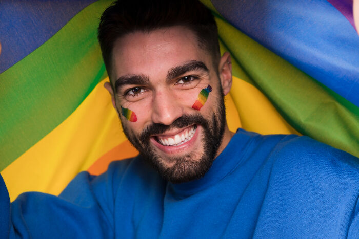 Smiling man with rainbow face paint and flag in background representing unexpected real life plot twists and family surprises.