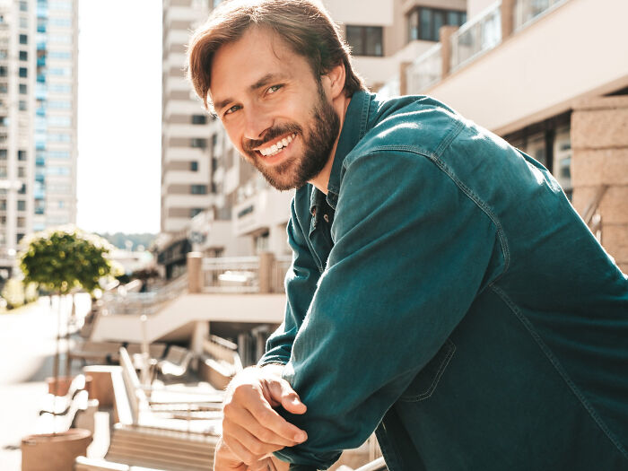 Smiling man leaning on railing outdoors in the city, representing real life plot twists involving family relationships.