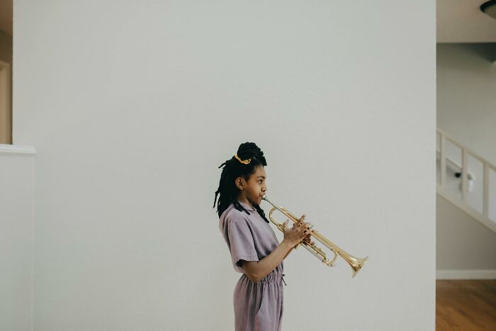 Young woman playing trumpet indoors, illustrating real life plot twists and unexpected family relationships.