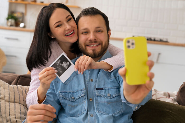 Couple happily taking a selfie while holding an ultrasound photo, representing surprising real life plot twists.