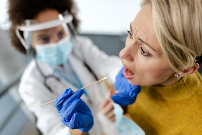 Medical professional wearing gloves and mask swabbing a surprised woman’s throat, illustrating real life plot twists.