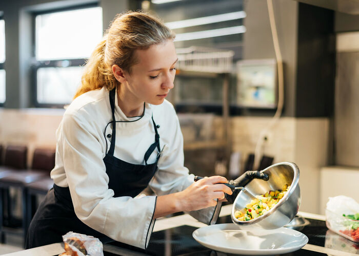 Young female chef preparing a dish in a professional kitchen, illustrating unexpected real life plot twists.