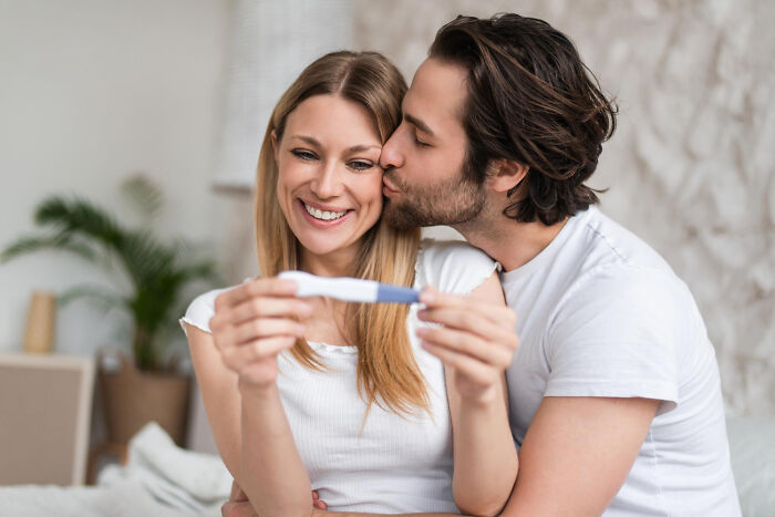 Couple hugging and smiling while holding a pregnancy test, depicting real life plot twists and surprising family moments.