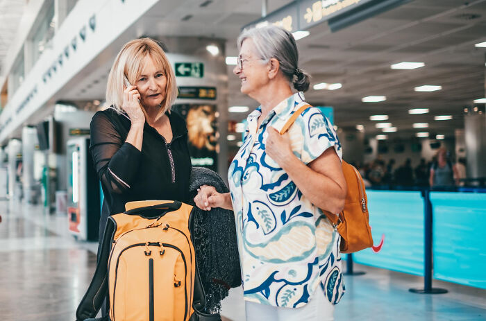 Two women talking at an airport with luggage, illustrating real life plot twists and surprising family connections.
