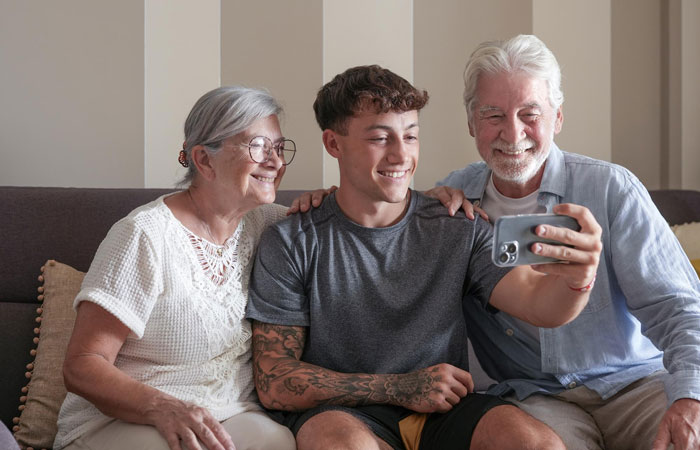 Teen son taking a selfie with elderly grandparents at home, reflecting family dynamics in a tense situation about raising a baby.