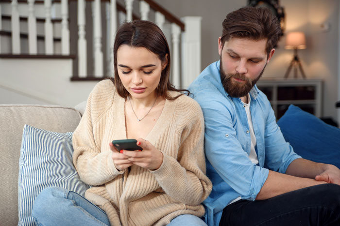 Couple sitting apart on couch during a tense moment, boyfriend uneasy about girlfriend&rsquo;s bond with male best friend.