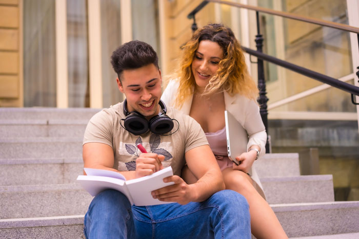 Young man and woman sitting on steps, smiling and interacting, highlighting gf confused after bf finds male bestie connection problematic.