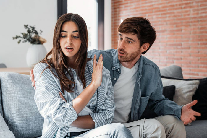 Young couple in a tense conversation on couch, girlfriend confused about boyfriend finding her male bestie connection problematic.