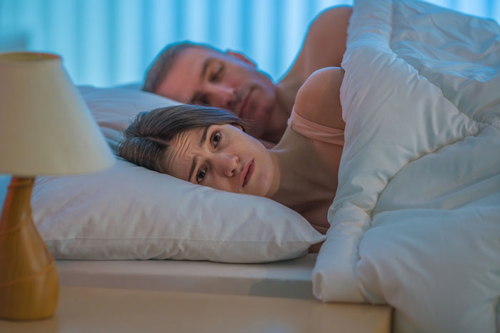 Worried woman lying in bed beside man, reflecting tension from dangerous traps and suspicion in their home relationship. Worried woman lying in bed beside man, reflecting tension from dangerous traps and suspicion in their home relationship.