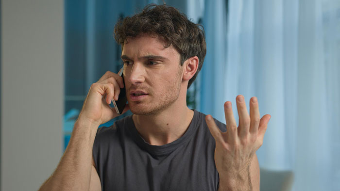 Young man looking frustrated while talking on the phone, depicting possessive family conflict at birthday party.