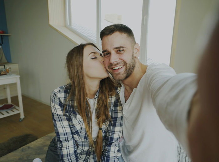 A woman kisses a smiling man on the cheek, taking a selfie. This image relates to stories about divorce papers and baby bumps.