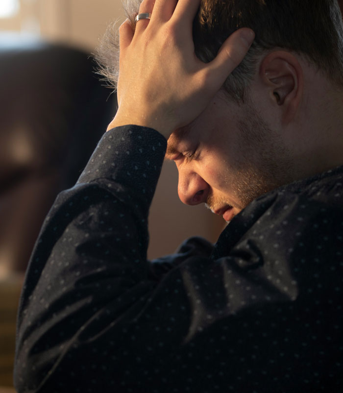 A distressed man with a ring on his finger holds his head in his hands, facing the challenge of divorce papers.