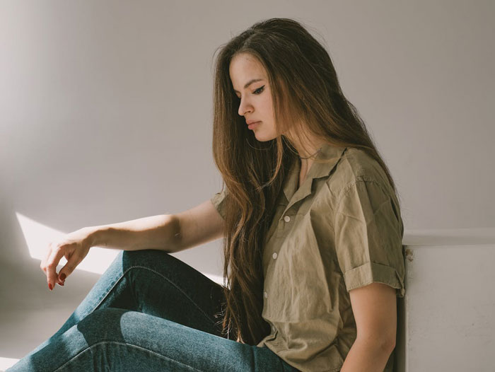 A young woman with long brown hair, sitting dejectedly. Her pose reflects distress, possibly about divorce papers or a baby bump.