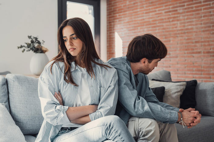 Couple sitting apart on couch looking upset, illustrating a boyfriend caught in a wedding lie exposing secret life.