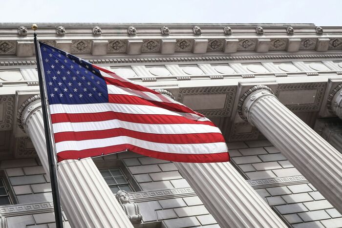 American flag flying in front of a classical building with columns representing PR mistakes and company backfire risks.