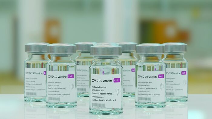 Clear glass vials labeled COVID-19 vaccine arranged on a reflective surface with a blurred background.