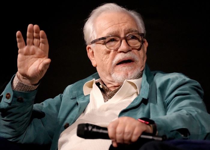 Brian C*x speaking passionately while holding a microphone, facing backlash after a brutal dig at actors.