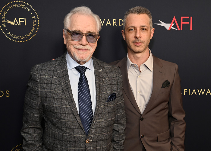 Brian C*x at an AFI event wearing a checkered suit and sunglasses facing backlash after brutal dig controversies.