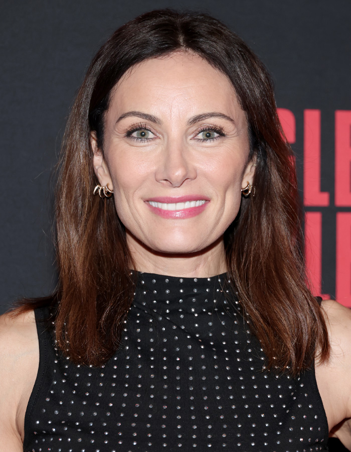 Broadway star with brown hair and earrings smiling at event, reflecting celebrity trolling after plane recognition complaint.