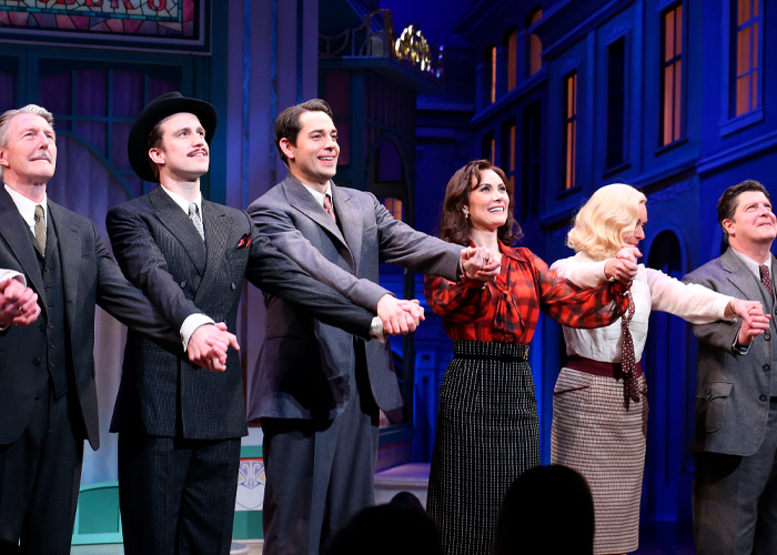 Broadway star and cast members holding hands on stage during final curtain call, spotlight highlighting their smiles.