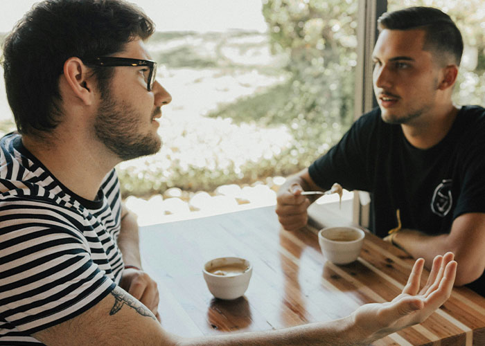 Two men having a conversation over coffee, illustrating a man thinking his best friend working as a server is low. Two men having a conversation over coffee, illustrating a man thinking his best friend working as a server is low.