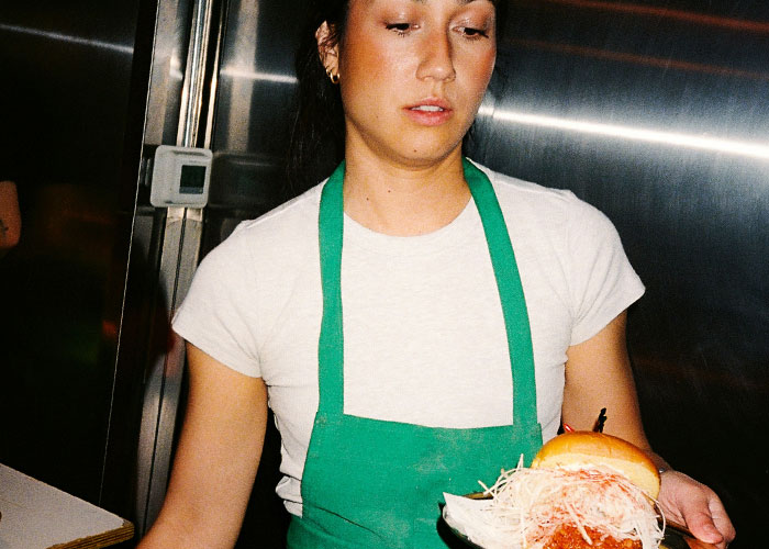 Server wearing a green apron holding a plate with a sandwich, highlighting perceptions of working as a server. Server wearing a green apron holding a plate with a sandwich, highlighting perceptions of working as a server.