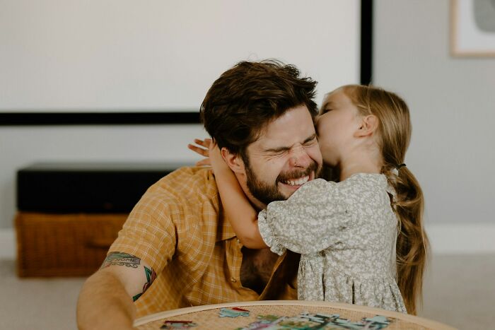 A joyful dad raising daughters, smiling as his young daughter gives him a kiss on the cheek.