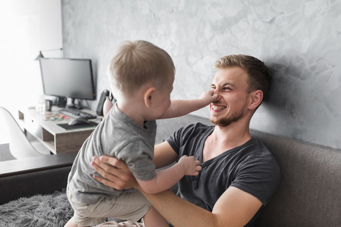 A joyful young dad on a couch, smiling as his son playfully pokes his nose. A loving family moment for father and son. A joyful young dad on a couch, smiling as his son playfully pokes his nose. A loving family moment for father and son.