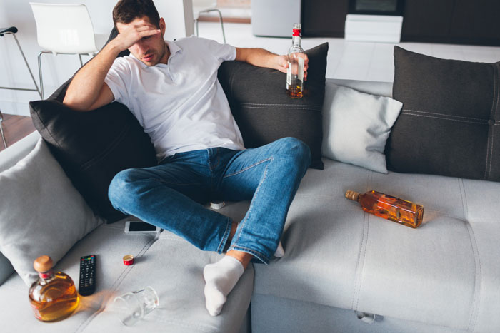 Distraught dad sits on a couch, holding a bottle, surrounded by alcohol. He looks like he went from dad to uncle. Distraught dad sits on a couch, holding a bottle, surrounded by alcohol. He looks like he went from dad to uncle.