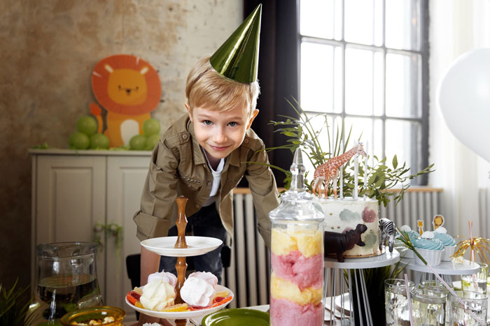 A boy in a party hat smiles at a safari-themed birthday party table, ready to prove DIL is too sensitive.