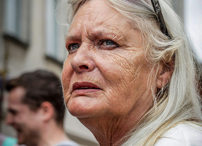 Mulher idosa de cabelos brancos parecendo chateada durante uma disputa de estacionamento envolvendo um homem e intervenção policial.