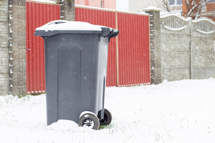 Gray outdoor bin covered with snow in a snowy yard, illustrating man getting revenge on honking driver with ice-filled bin.