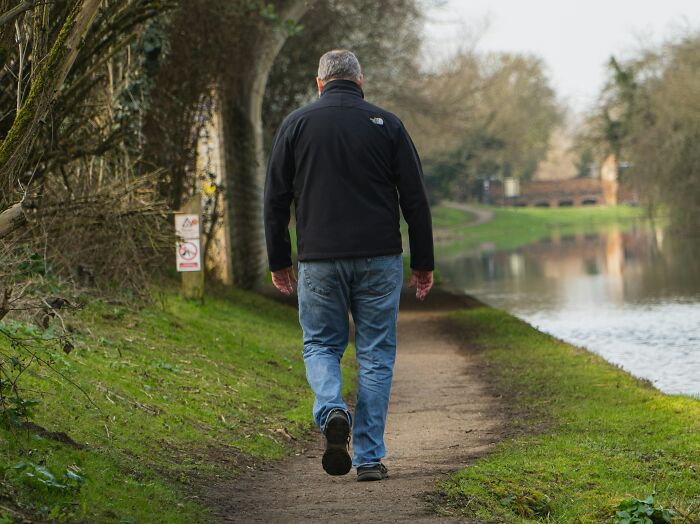 Man walking alone on a narrow path beside a river in a peaceful outdoor setting related to urban legends.