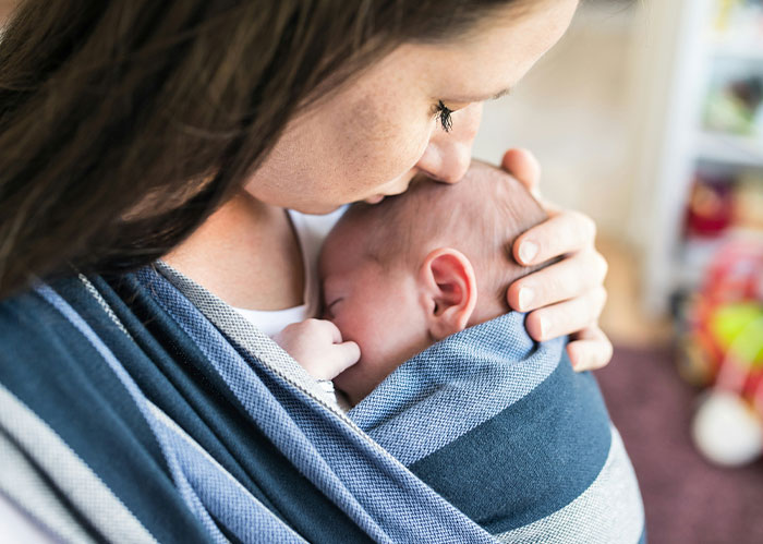 Woman gently holding a baby close in a wrap, capturing a tender moment unrelated to police chasing the wrong person stories