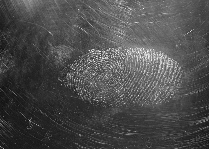 Close-up of a fingerprint on a textured dark surface, symbolizing police chasing the wrong person in wild stories.